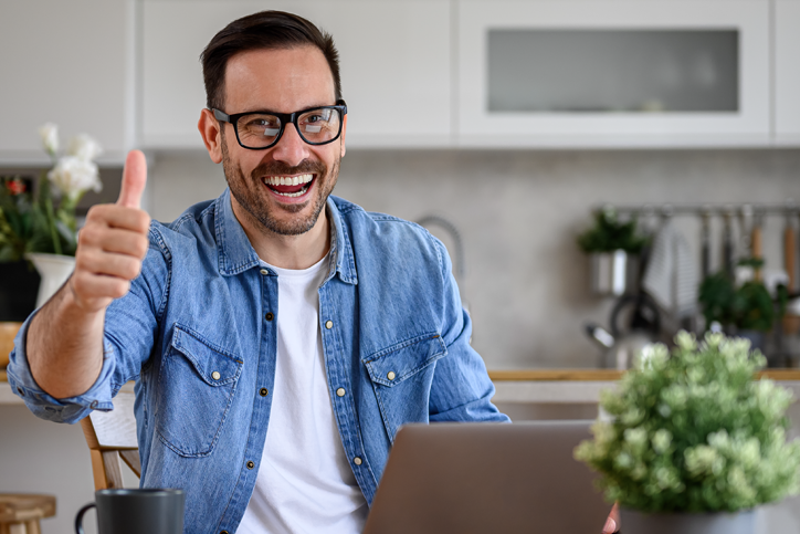 Guy on laptop in kitchen giving a thumps up